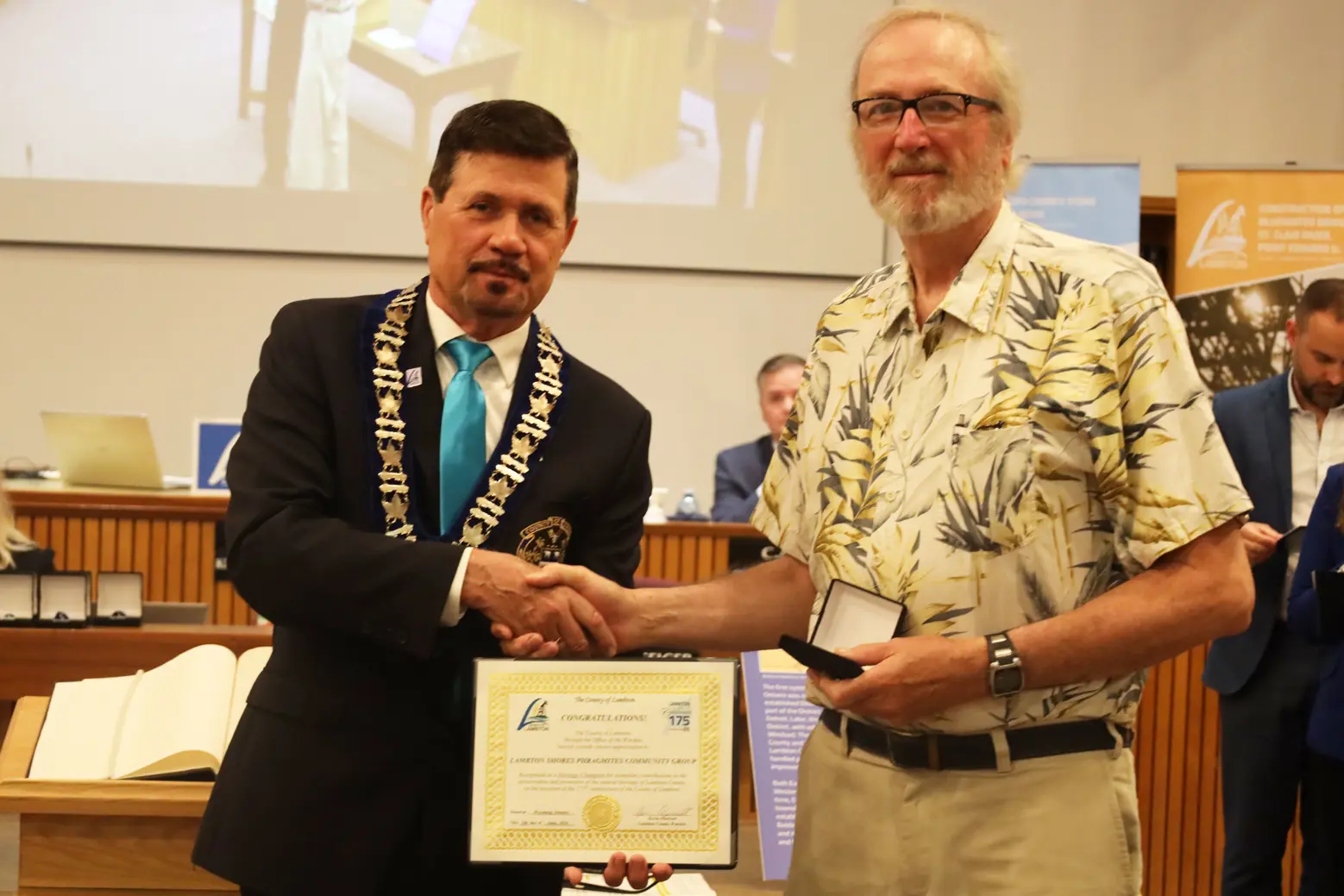 Photo of a man in collared shirt accepting certificate from another man with brown hair.