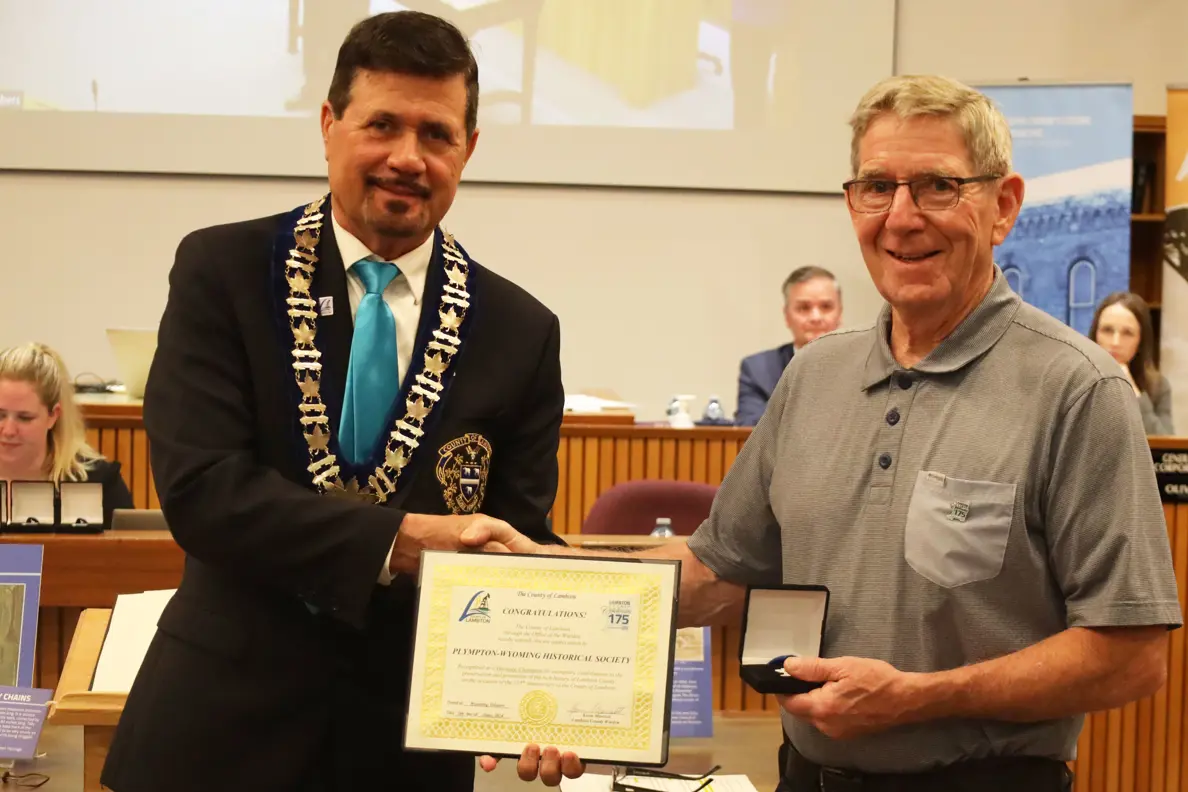 Photo of a man in collared shirt accepting certificate from another man with brown hair.