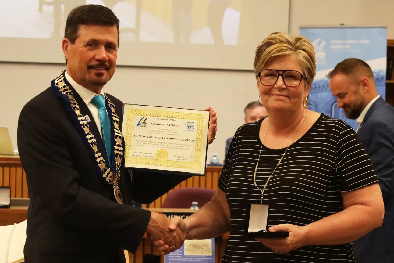 Photo of a woman in a striped shirt accepting an award from a man in a suit.