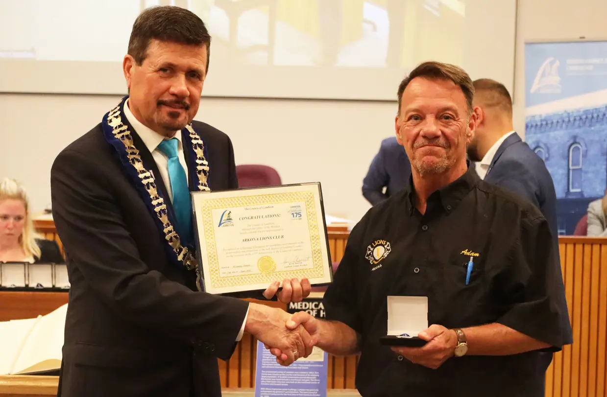 Photo of a man in collared shirt accepting certificate from another man with brown hair.