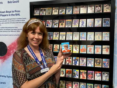 CuratorSupervisor-Dana-Thorne-holds-her-personal-hockey-card-in-front-of-a-display-in-the-Hockey-exhibit-web.png