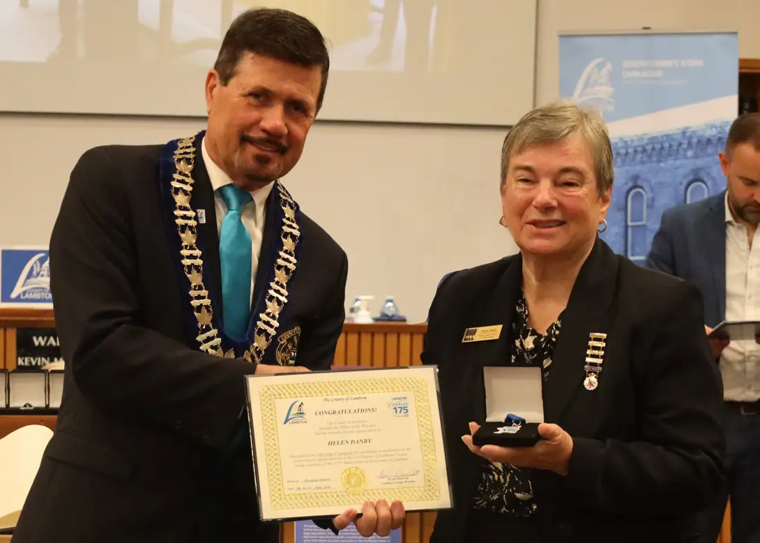 photo of a white woman in a suit accepting an award from a man in a suit.