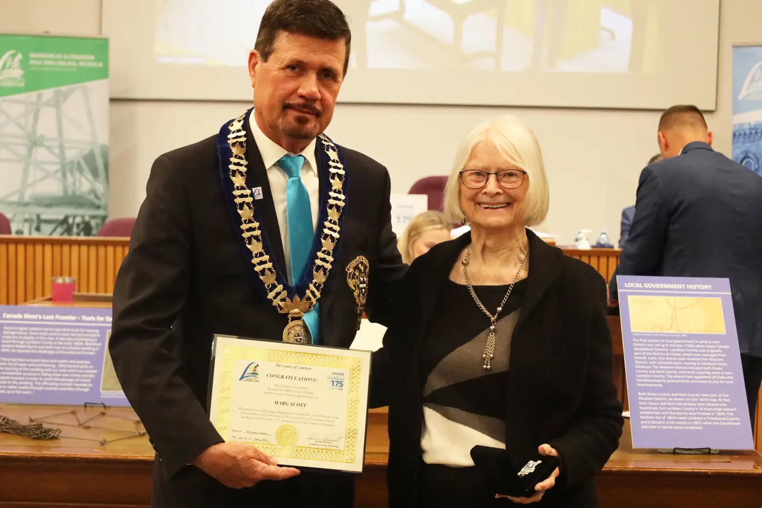 photo of a woman in a suit accepting an award from a man in a suit.