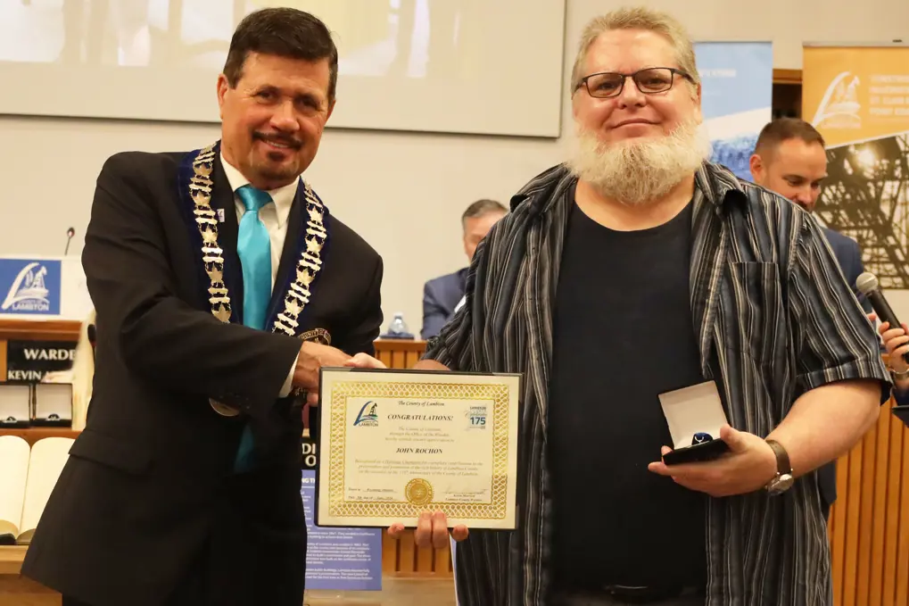 Photo of a man with white hair accepting certificate from another man with brown hair.