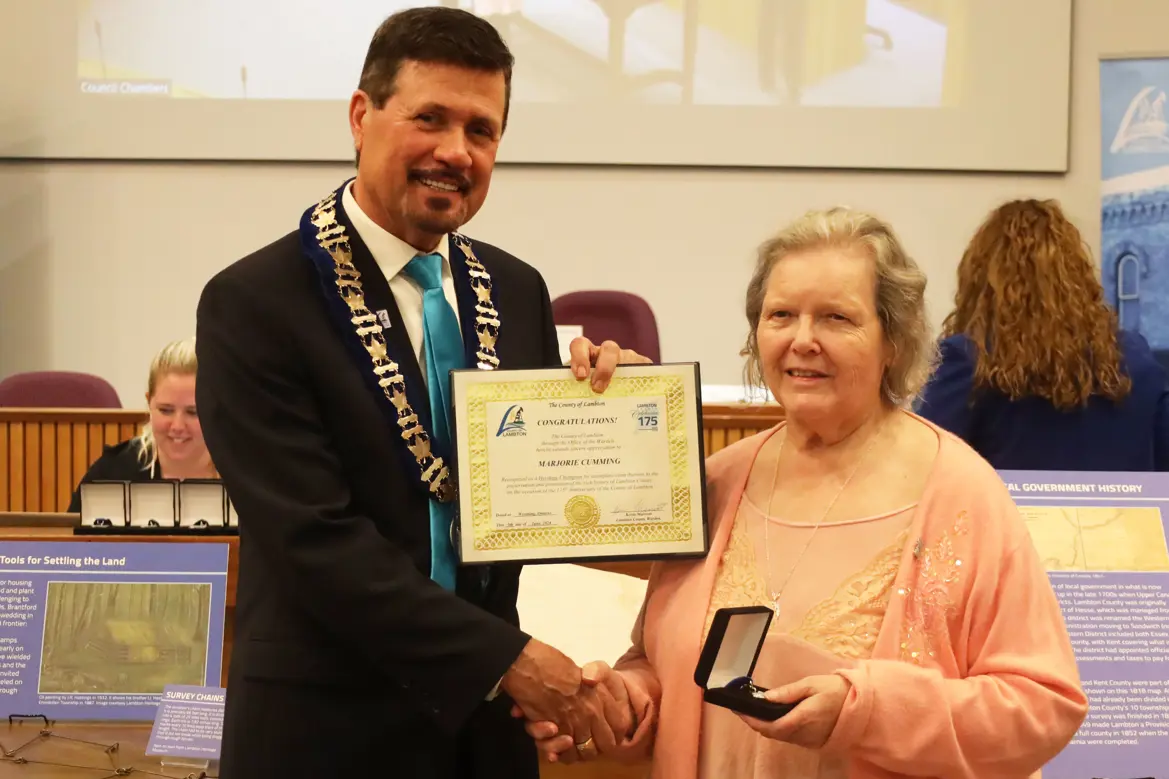 Photo of a woman in pink shirt and sweater accepting an award from a man in a suit.