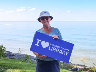 Gwen-Moore-a-library-patron-holds-an-I-Love-Lambton-County-Library-sign-at-Brights-Grove.jpg