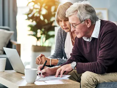 older-couple-filling-out-paperwork-on-a-coffee-table-in-front-of-a-laptop-web.jpg